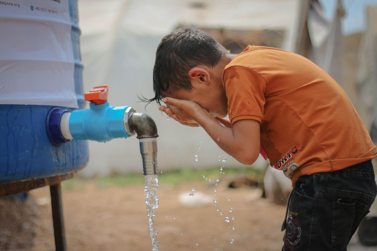 services-03 A young boy cools off by splashing water from an outdoor faucet on a hot summer day in Idlib, Syria.