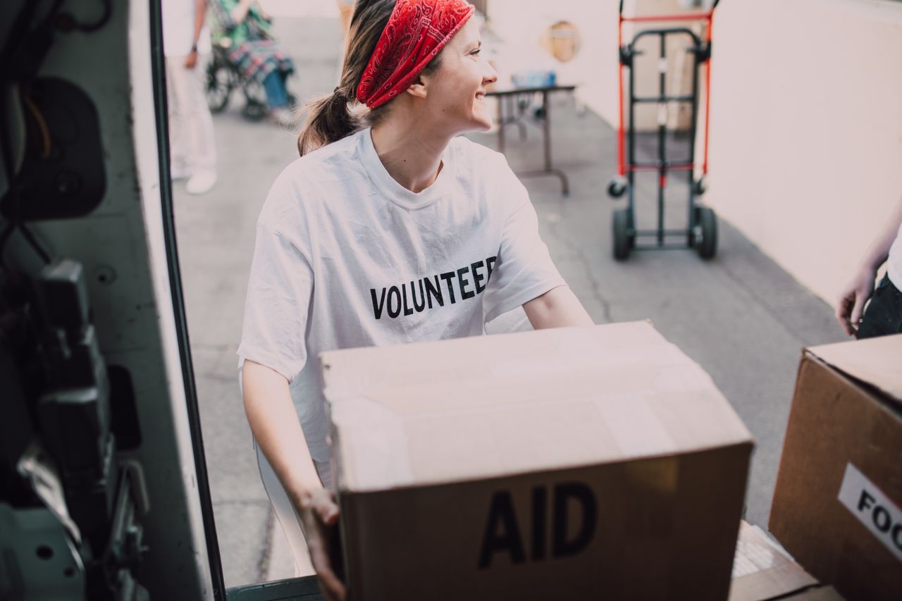 Smiling volunteer woman carrying aid boxes for a charity event.